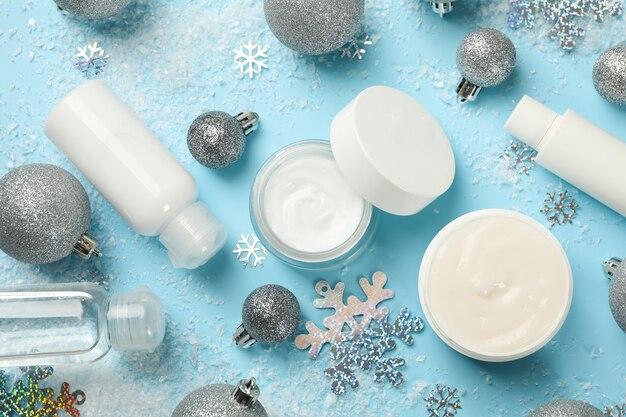 Skincare products with festive holiday decoration including silver ornaments and snowflakes on a light blue background