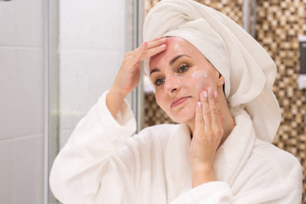 Woman in bathrobe applying facial cream in bathroom